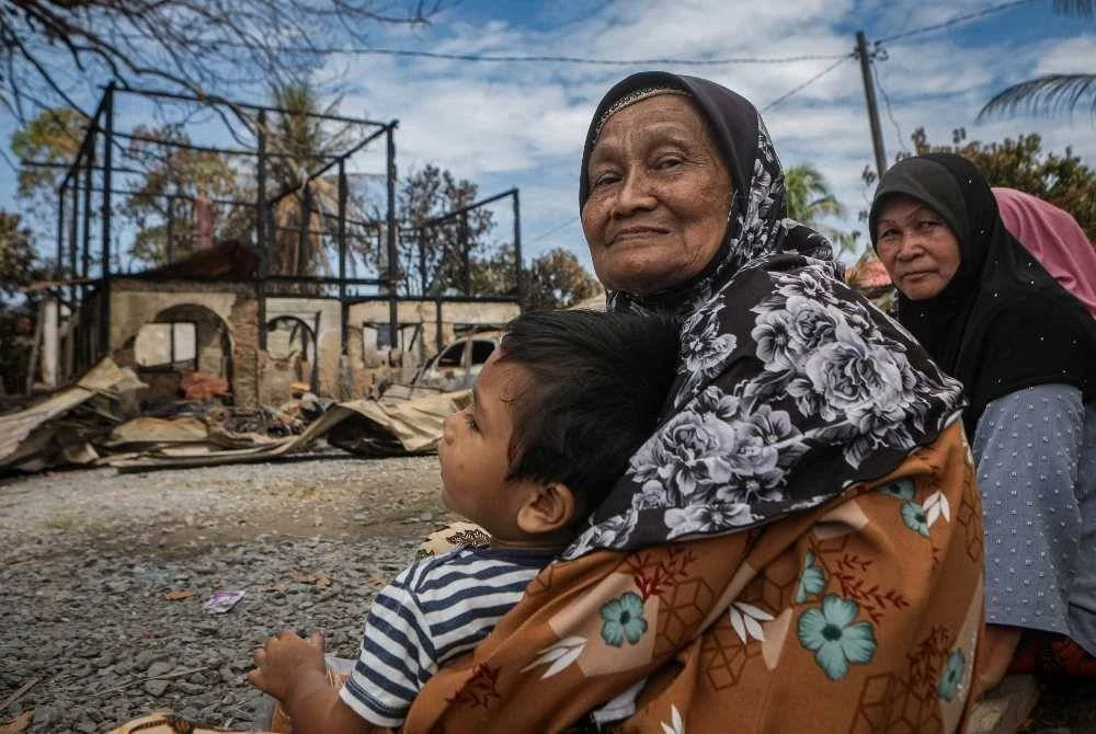 Manis di hadapan rumahnya yang musnah dalam kebakaran di Kampung Sungai Padang, Simpang Empat pada Khamis. FOTO: Bernama