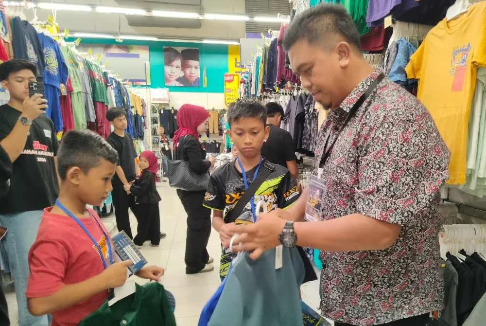 Mohd Nazari (kanan) membantu memilih pakaian dan kelengkapan Aidilfitri buat anak-anak yatim yang dibawa dari kawasan Parlimen Pasir Salai di Pasar raya Besar Mydin Meru Raya di sini pada Ahad.