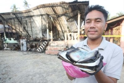 Muhamad Syamrul Nazrel menunjukkan wang dalam al-Quran dengan kesan terbakar, namun dipercayai masih boleh ditukar di bank dengan wang baharu.
