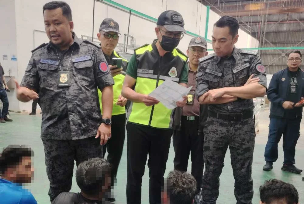 Khairrul Aminus (tengah) memeriksa dokumen pekerja asing dalam serbuan di sebuah gudang di Shah Alam pada Selasa.