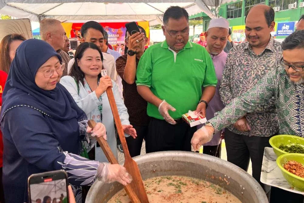 Fuziah (kiri) bersama Mas Imran (tengah) mengacau bunur lambuk yang bakal diedarkan kepada pengunjung yang hadir ke Econsave Balakong.