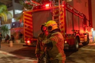 Anggota bomba beroperasi di luar bangunan terkena peluru berpandu di pinggir Tel-Aviv. Foto: AFP
