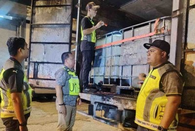 Mohd Shahran (dua dari kiri) memeriksa sebuah lori yang menempatkan tong IBC bagi membawa muatan minyak masak bersubsidi yang diseleweng dalam serbuan di Jalan Klang Lama, Kuala Lumpur pada Jumaat.