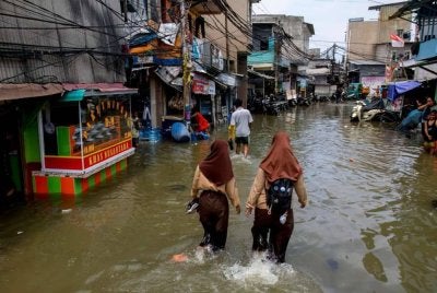 Dua pelajar perempuan meredah jalan di Muara Baru, Jakarta . - AFP