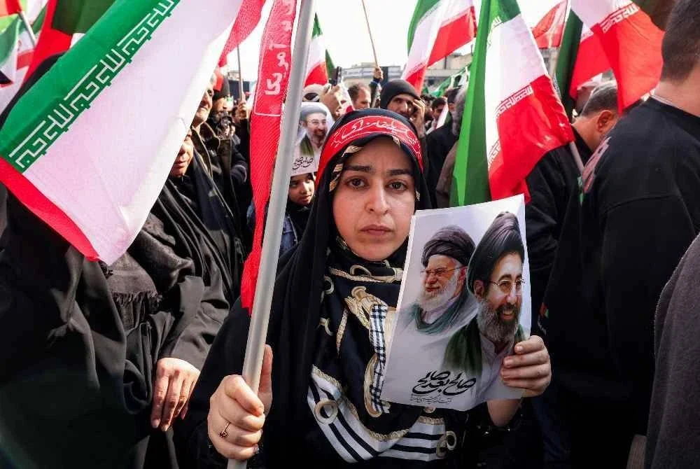 Seorang wanita memegang gambar Pemimpin Tertinggi Iran baharu, Mojtaba Khamenei bersama bapanya, Ali Khamenei ketika perhimpunan di Dataran Enghelab, Teheran. - AFP