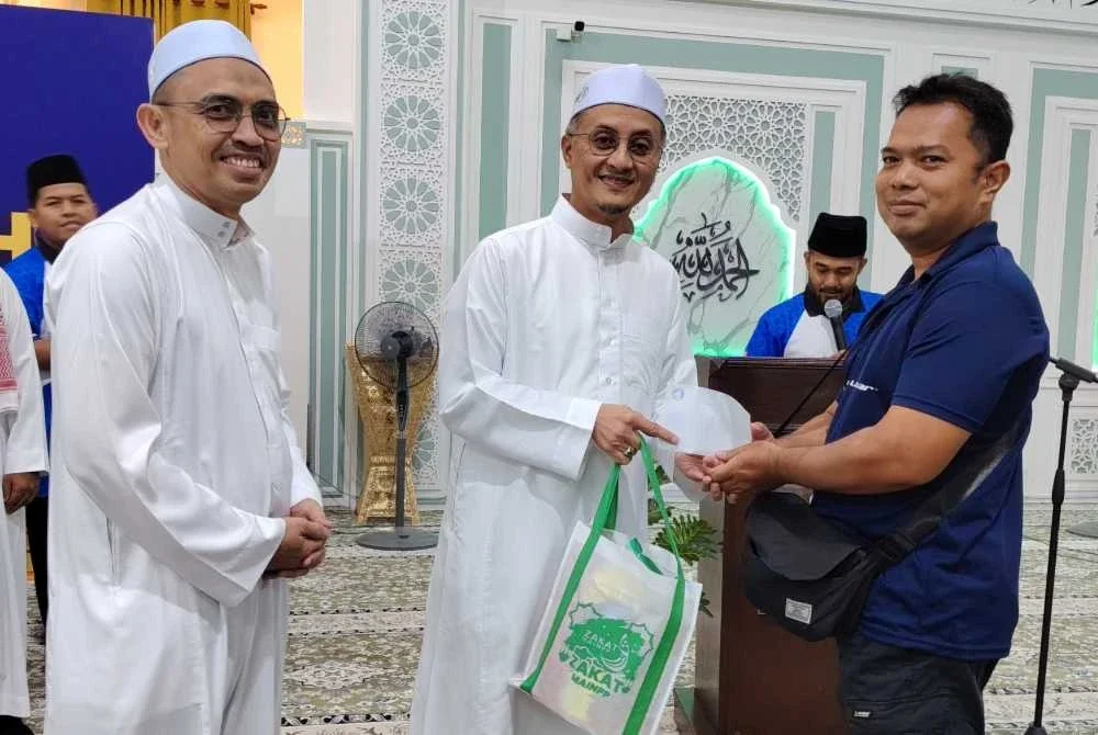 Mohamad (tengah) menyampaikan wang tunai RM300 serta hamper sumbangan Zakat Mart dan pek makanan berbuka puasa kepada salah seorang penerima.