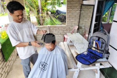 Muhammad Irfan Fikry tekun memotong dan merapikan rambut seorang pelanggannya di Kuala Nerus.