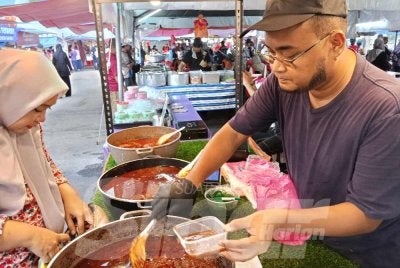 Amirul mencedok lauk nasi beriani kukus di gerainya di BazarRamadan Taman Perling.