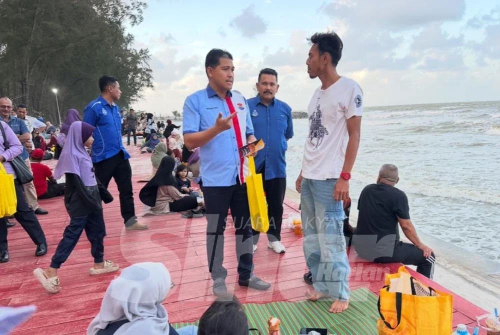 Ismail (kiri) memberi penerangan keselamatan kepada pengunjung pantai. Foto: ADILA SHARINNI WAHID