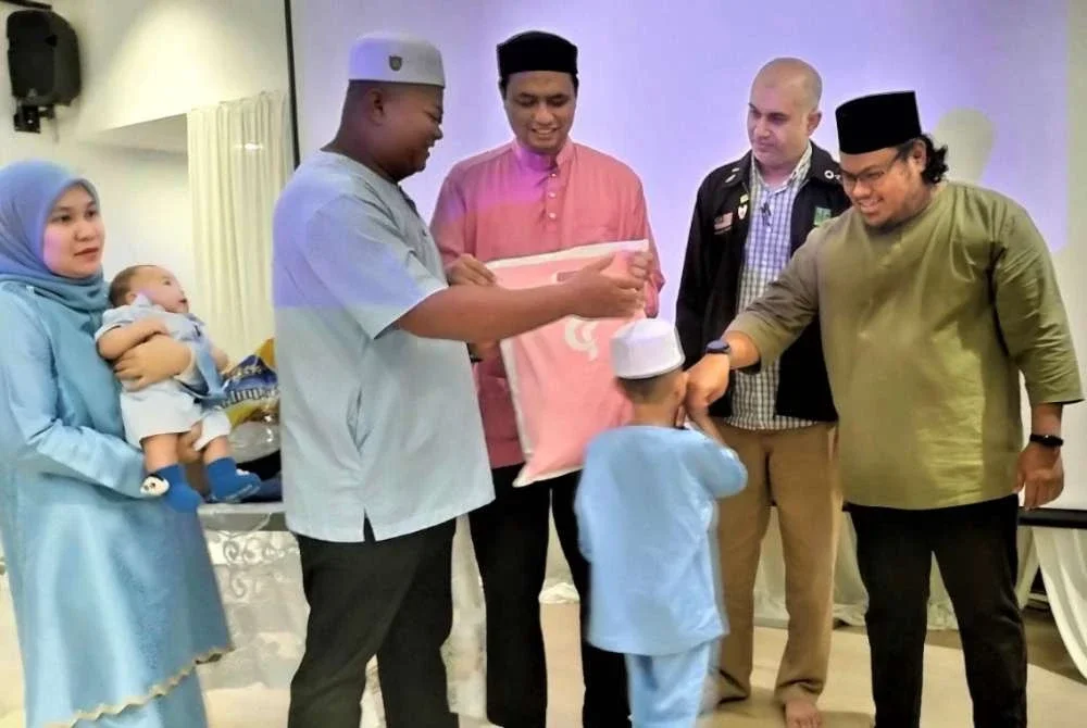 Izzat menyantuni anak klien AADK sementara diperhatikan oleh Viqar Mohamed, Pegawai Perhubungan MAPIM (jaket hitam) sementara Ketua Daerah AADK Daerah Petaling, Mohd Lathfi Rohman menyerahkan baju Raya kepada penerima sumbangan.