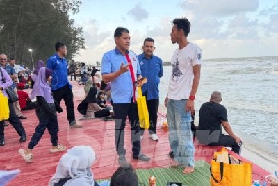 Ismail (kiri) memberi penerangan keselamatan kepada pengunjung pantai. Foto: ADILA SHARINNI WAHID