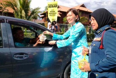 Sandrea (kiri) memberikan bubur lambuk kepada pengguna jalan raya sempena Majlis Edaran Bubur Lambuk Iftar Ramadan JBPM Perak di Bulatan Sultan Azlan Shah, Meru Raya, Ipoh pada Khamis.