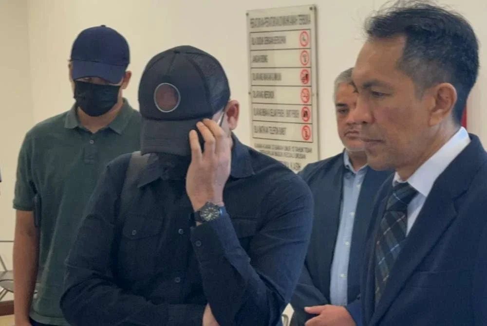 Khuzairi (dua dari kanan) berpakaian serba hitam, berpelitup muka dan mengenakan topi hadir ke Mahkamah Sesyen Shah Alam pada Jumaat, atas tiga pertuduhan menerima RM13,000 daripada seorang usahawan teknologi, lapan tahun lalu.