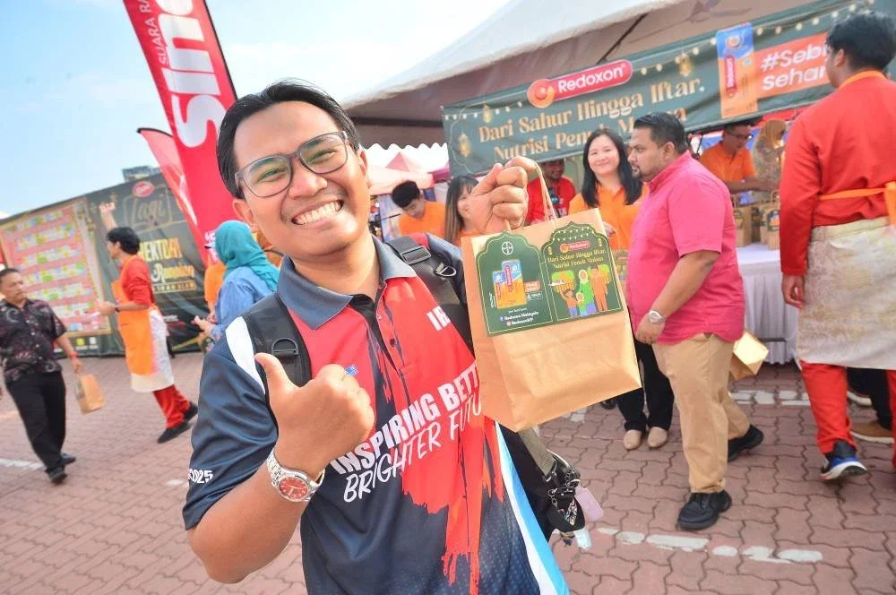 Seorang pengunjung bazar gembira menerima pek makanan di reruai Redoxon.