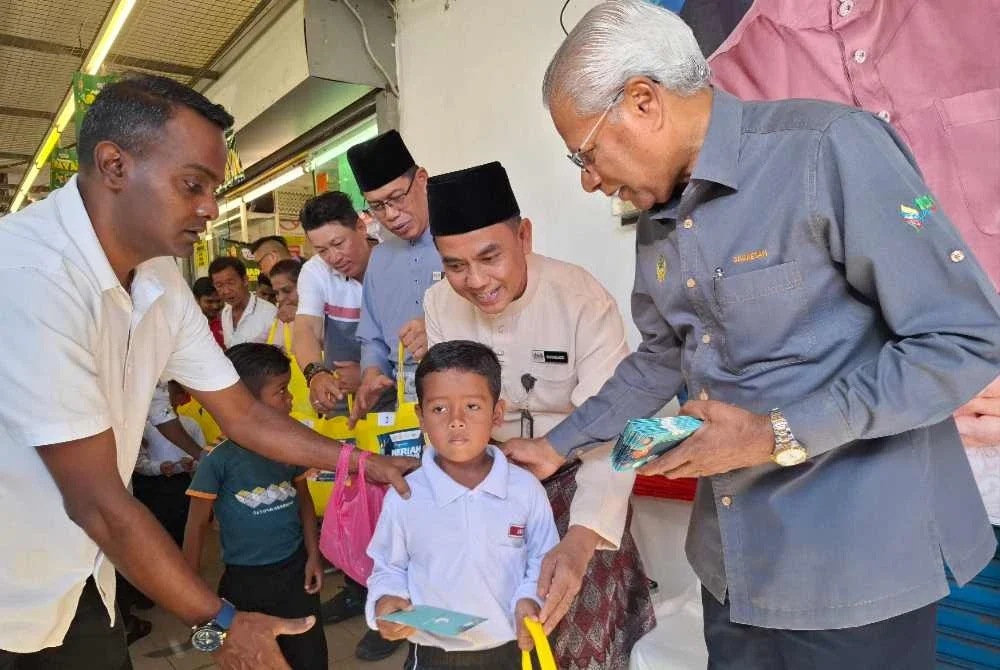 Sivanesan (kanan) menyempurnakan penyerahan baju raya kepada 150 pelajar terpilih di hadapan Pasar Raya TenTen Bidor pada Jumaat.