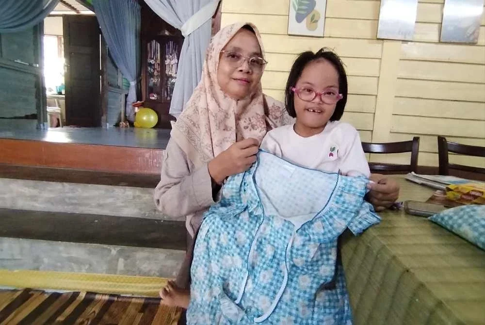 Arissa Imani (kanan) yang merupakan penghidap Sindrom Down menunjukkan baju tidur arwah kakaknya yang maut dalam nahas bas diKilometer 53, Jalan Raya Timur-Barat (JRTB) Jeli-Gerik pada 9 Jun tahun lalu.
