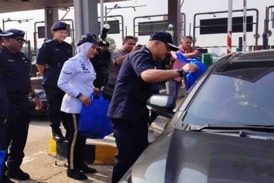 Azizee menyerahkan 'goodies' kepada pemandu kereta yang melalui Plaza Tol Juru di Bukit Mertajam, pada Rabu.