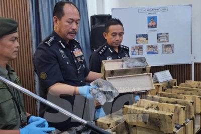 Jauteh (tengah) menunjukkan dadah yang disorokkan dalam bongkah kayu atau kotak botol arak dalam sidang akhbar di IPK Sabah.