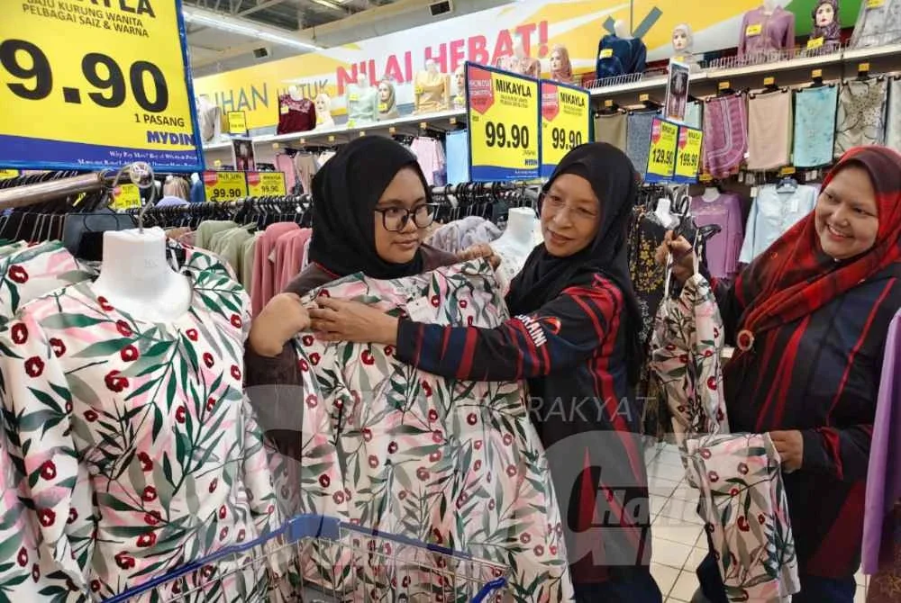 Nurin Amira Aleya (kiri) dibantu Zuraini (tengah) semasa memilih baju raya di pasar raya Mydin di Alor Setar.