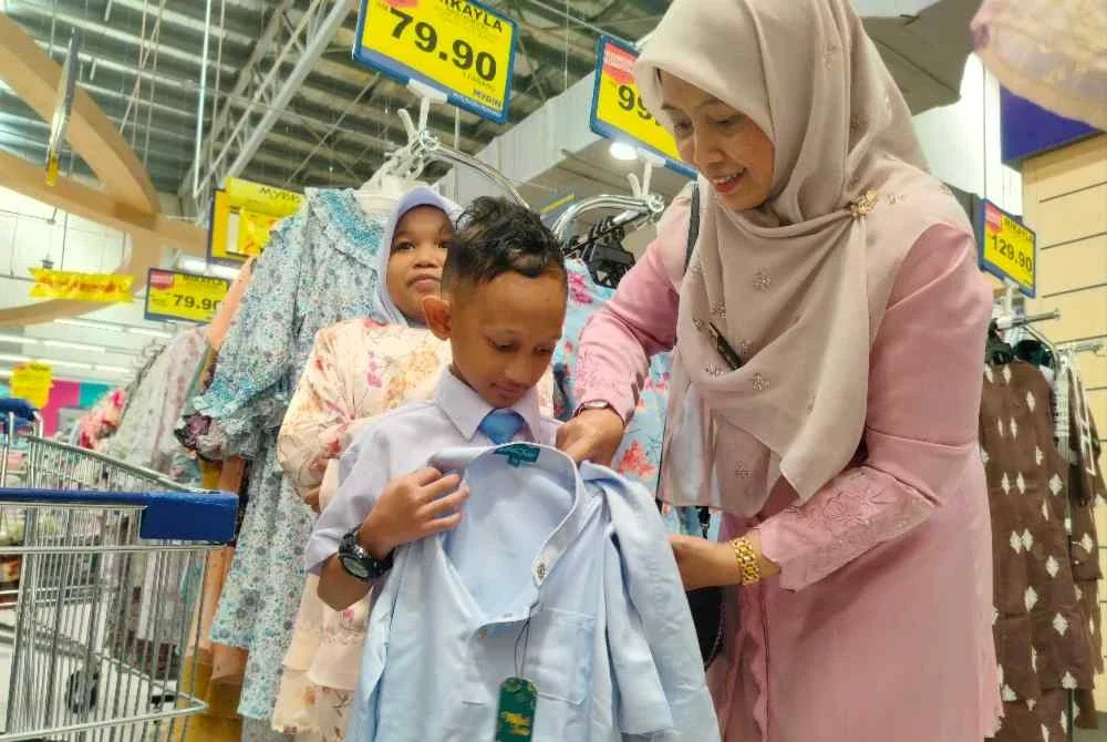 Lily Hafidza (kanan) membantu memilih pakaian hari raya buat dua orang anak muridnya di Pasar raya Besar Mydin Meru Raya di sini baru-baru ini.