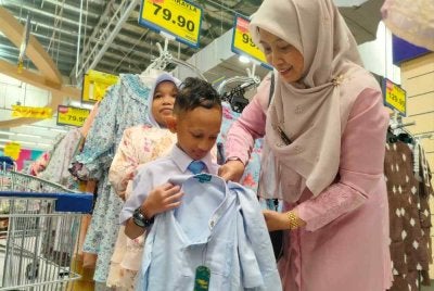 Lily Hafidza (kanan) membantu memilih pakaian hari raya buat dua orang anak muridnya di Pasar raya Besar Mydin Meru Raya di sini baru-baru ini.