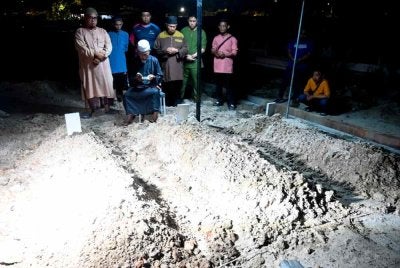 Imam Surau Ar-Rahman, Fadli Abdullah (duduk) membacakan talkin setelah ketiga-tiga jenazah tiga beranak dikebumikan di Tanah Perkuburan Islam Batu 6, Bakri, di sini, tengah malam tadi. Foto Bernama
