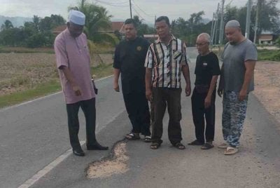 Zainol Abidin (kiri) bersama penduduk menunjukkan keadaan laluan jalan Kuala Nerang - Changlun yang tidak rata.