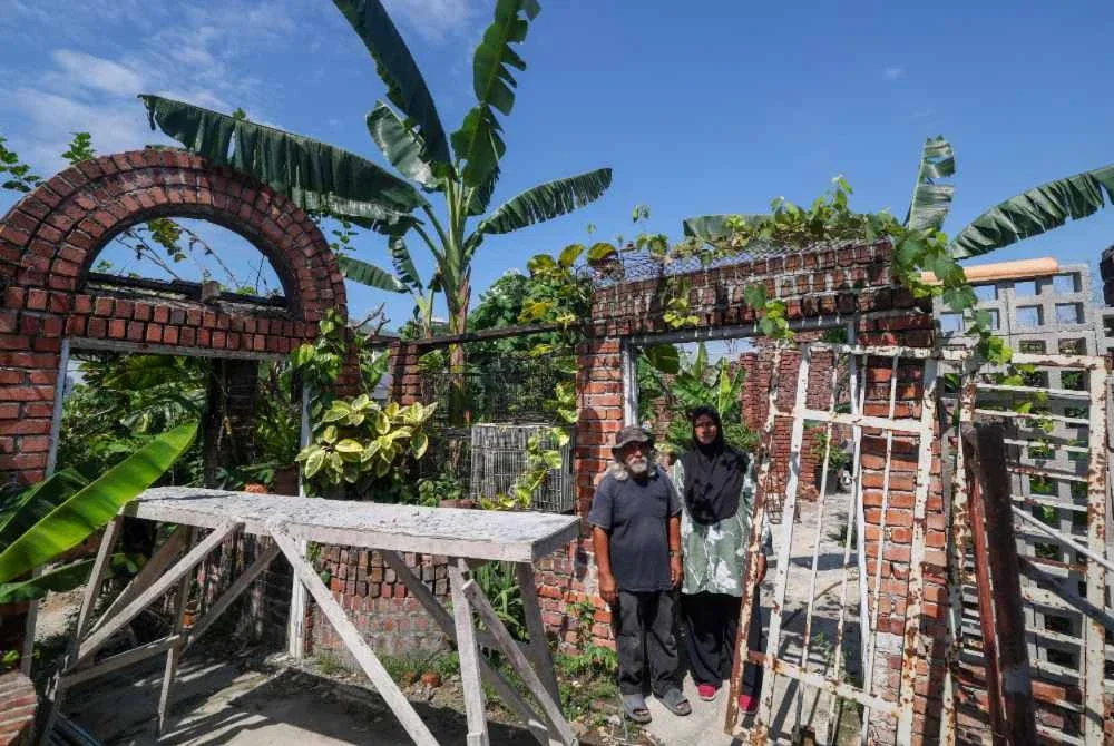 Mohamad Nasir bersama isterinya, Aliyah di hadapan bekas rumah mereka yang musnah akibat tragedi letupan gas di Taman Putra Harmoni tahun lepas. Foto Bernama