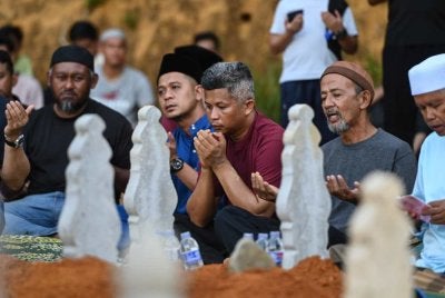 Mohamad Redzuan Abdullah mengaminkan doa ketika pengebumian isteri serta dua anaknya di Tanah Perkuburan Islam Kampung Sungai Tong, Setiu pada Selasa. Foto Bernama