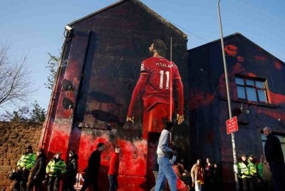 Peminat melintasi mural Mohamed Salah berhampiran Anfield. 