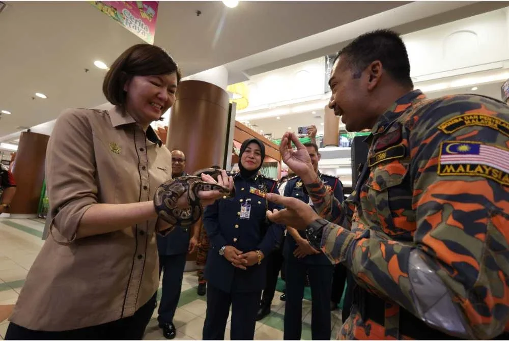 Sandrea (kiri) memegang seekor ular sawa dalam Program Kesedaran Keselamatan Awam sempena Program Satelit Program Madani Rakyat anjuran JBPM Perak di AEON Mall Kinta City di Ipoh pada Ahad.