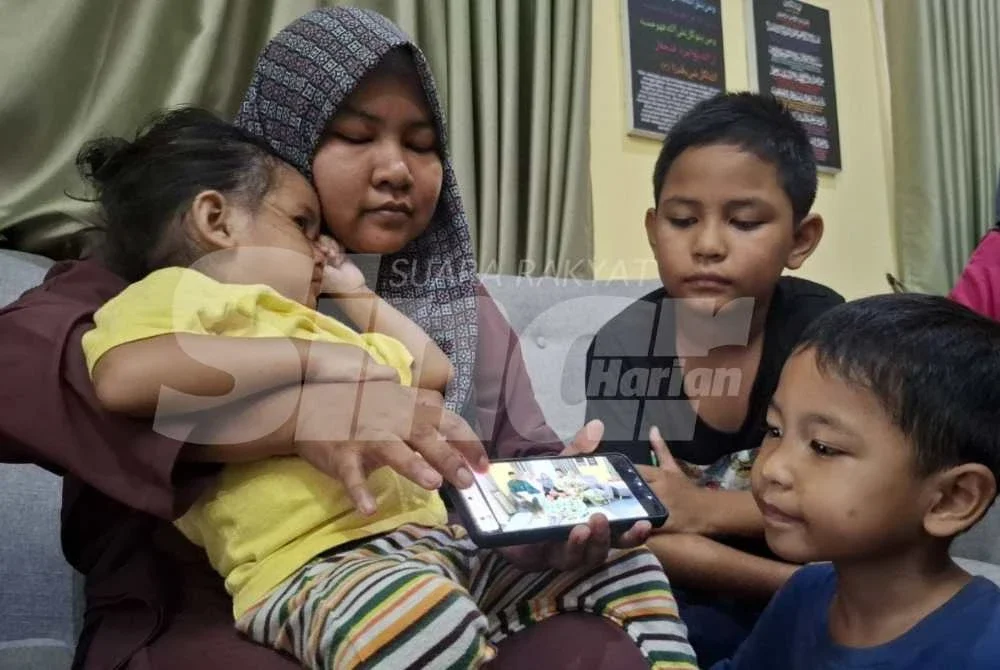 Nor Nadia (tengah) menunjukkan gambar kenangan mereka sekeluarga ketika menyambut Aidilfitri baru-baru ini.