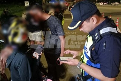 Pegawai JPJ sedang memeriksa dokumen penunggang motosikal yang ditahan dalam operasi dijalankan.