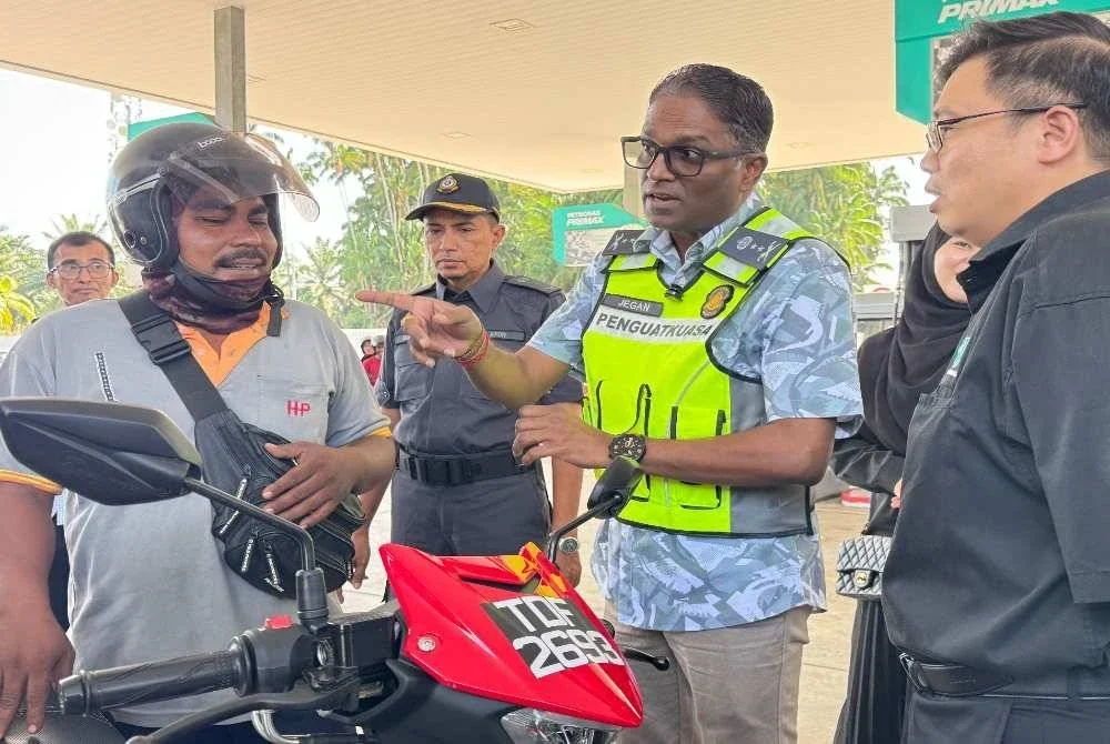 Jegan (dua dari kanan) menerangkan mengenai larangan penjualan dan pembelian petrol RON95 kepada salah seorang penunggang motosikal di Stesen Petronas Sungai Dua di Butterwoth pada Khamis.