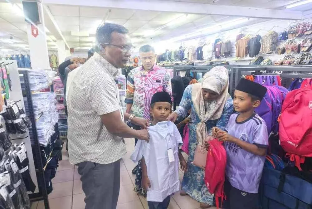 Zuraidi (kiri) membawa dua beradik yang keciciran sekolah membeli kelengkapan sekolah di sebuah pasar raya di Kuala Nerang pada Rabu.