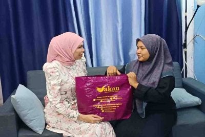 Riza (kiri) menyerahkan bantuan kepada Nor Nadia ketika ditemui di kediamannya pada Jumaat.