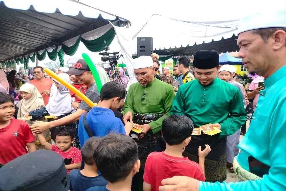 Idris (tiga dari kanan) menyampaikan duit raya kepada kanak-kanak yang hadir sempena Jamuan Terbuka Hari Raya Aidilfitri Pas Perak di Kompleks Pendidikan Islam Darul Muttaqin, Malim Nawar di sini pada Ahad.