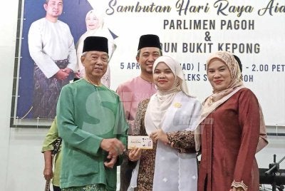 Muhyiddin (kiri) menyampaikan sumbangan kepada pelajar cemerlang SPM Parlimen Pagoh di Kompleks Belia Sukan Pagoh pada Ahad.