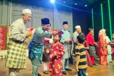 Ahmad Faizal (dua dari kiri) menyampaikan duit raya kepada kanak-kanak yang hadir ke Majlis Rumah Terbuka Aidilfitri Bersatu Negeri Perak bersama Bersatu Bahagian Sungai Siput di Pusat Konvensyen Tun Samy Vellu di sini pada malam Ahad.