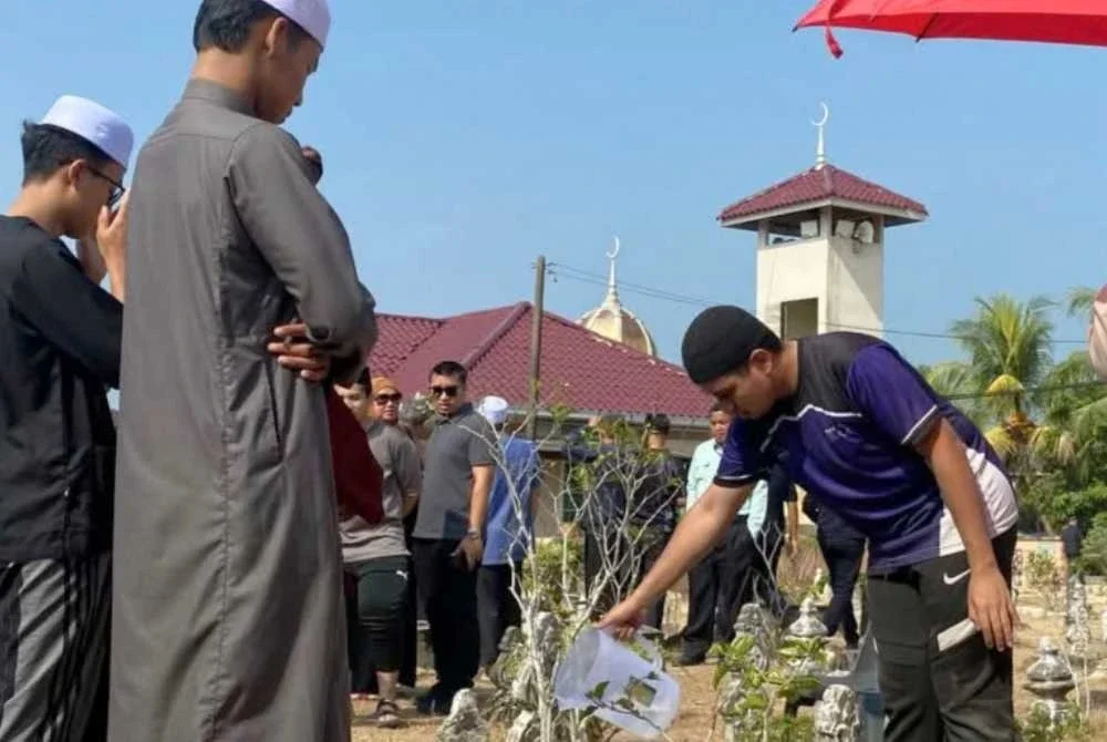 Anak arwah menyiram tanah perkuburan Allahyarham Azman yang dikebumikan di Tanah Perkuburan Islam Kampung Kuin Pasir, Bachok pada Selasa.