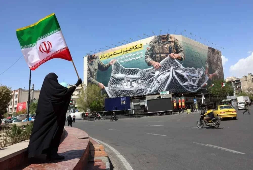Seorang wanita memegang bendera Iran berhampiran papan tanda bertulis Selat Hormuz kekal ditutup di Dataran Enqelab, Teheran.-AFP