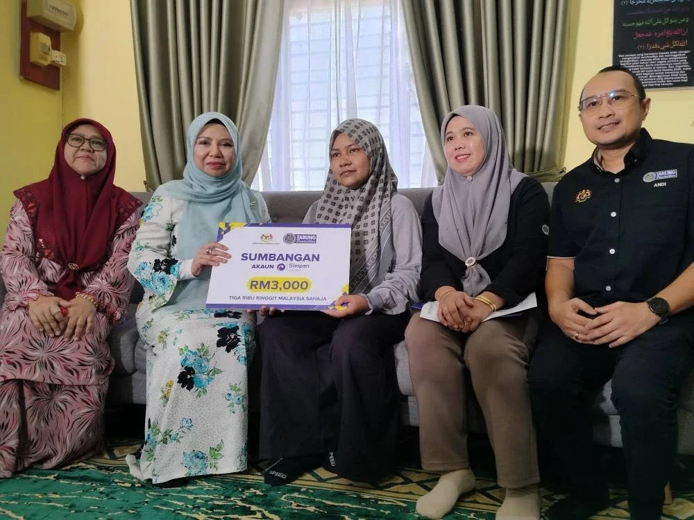 Norliza (dua dari kiri) menyerahkan sumbangan berjumlah RM3,000 kepada Nor Nadia (tengah) ketika Program Ziarah Kasih PTPTN di Kampung Repoh di sini pada Selasa.