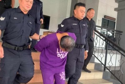 Tertuduh (tengah) diiringi polis ketika hadir ke Mahkamah Sesyen Lahad Datu pada Rabu.