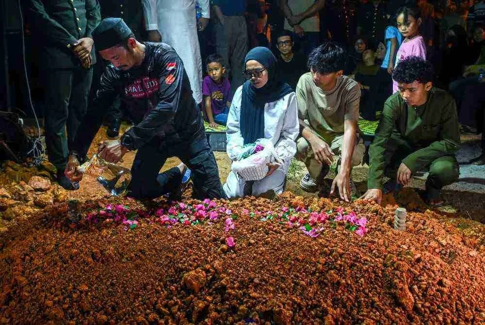 Rosafindi Tambi Chik (kiri) bapa kepada Allahyarham Muhammad Amirul Raziq menyiram air mawar di pusara anaknya selepas disemadikan di Tanah Perkuburan Felda Sungai Kelamah, Gemas, malam tadi. Foto Bernama
