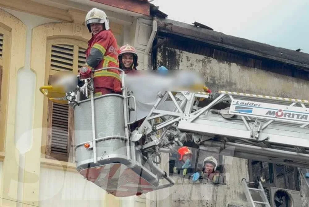 Anggota bomba menurunkan mayat mangsa pertama dari tingkat satu bangunan yang terbakar dalam kejadian petang Isnin.