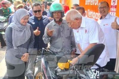 Mahdzir membantu mengisi minyak ke dalam motosikal pengguna ketika perasmian Stesen Minyak Mudah Alih di Desa Keda Sungai Tengas pada Isnin.