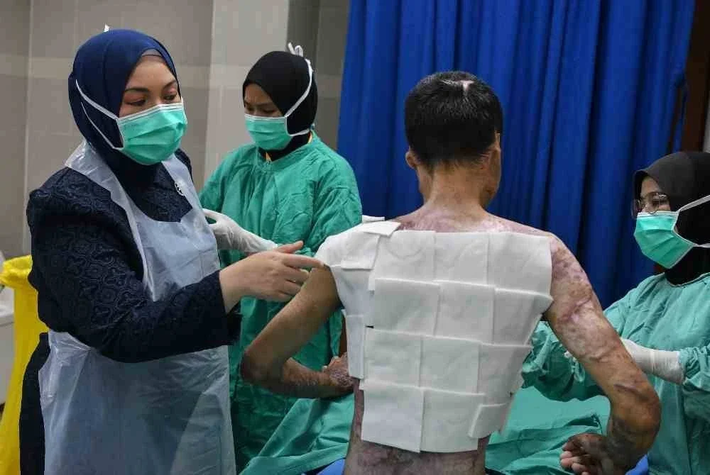 Penyelaras Unit Sains Rekonstruktif dan Koordinator Unit Rawatan Kebakaran (URK) Hospital Pakar Universiti Sains Malaysia (HPUSM), Dr Siti Fatimah Noor Mat Johar (kiri) menunjukkan rawatan yang diterima Ahmad Nasri Anwar, 31, kerana melecur teruk di HPUSM, baru-baru ini. Foto Bernama.