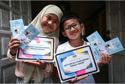 Aesha Khadeeja (kiri) dan adiknya, Uwais AlQorni (kanan) menunjukkan tablet dan duit raya daripada Perdana Menteri ketika ditemui di kediaman mereka di Ladang Titian pada Selasa. Foto Bernama