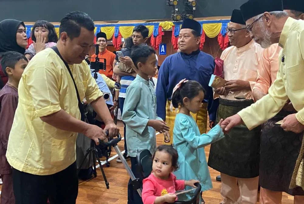 Khalid menyampaikan sumbangan duit raya kepada kanak-kanak yang hadir ke Majlis Ramah Mesra Pengerusi KADA, di Dewan Serbaguna Presint 8, di sini pada Rabu.