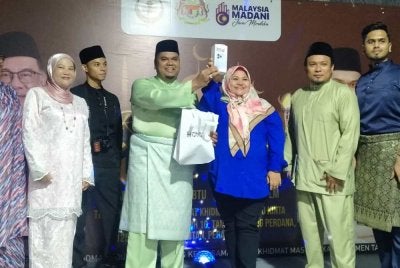 Muhamad Arafat (tengah) menyampaikan hadiah cabutan bertuah berupa sebuah telefon pintar kepada pengunjung sempena Majlis Rumah Terbuka Aidilfitri anjuran Pusat Khidmat Rakyat ADUN Hulu Kinta dengan kerjasama Parlimen Tambun pada Sabtu.